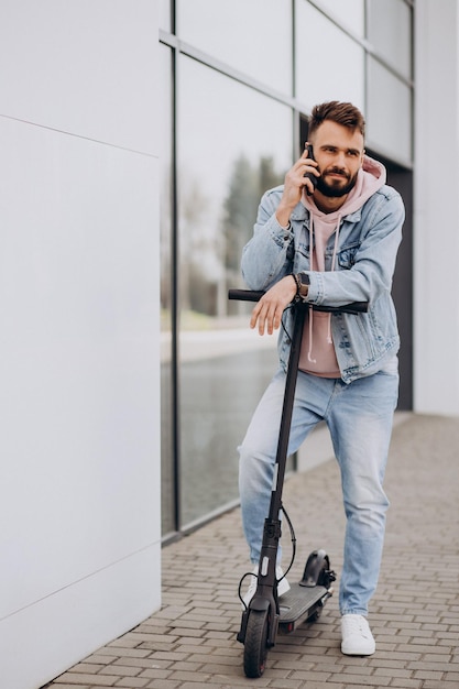 Giovane bello che guida uno scooter elettrico e utilizza il telefono