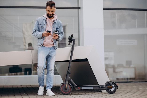 Giovane bello che guida uno scooter elettrico usando il telefono e bevendo caffè