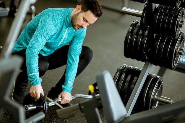 Giovane bello che prepara i dumbbells in ginnastica