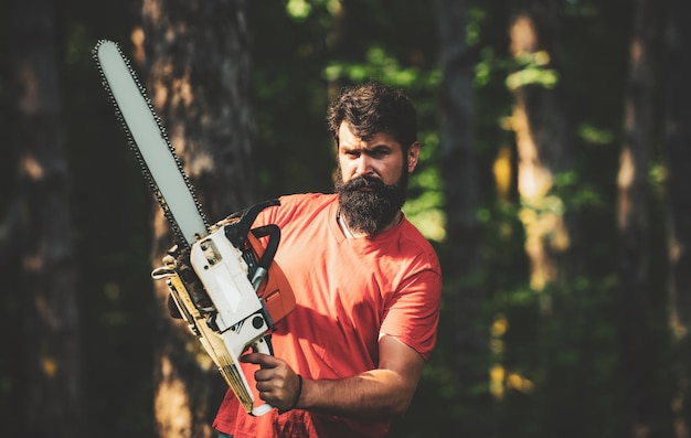 Giovane bello con l'ascia vicino al boscaiolo di deforestazione della foresta nei boschi con l'ascia della motosega agri