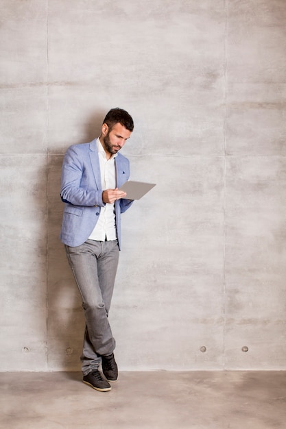 Giovane bello con tablet dal muro grigio