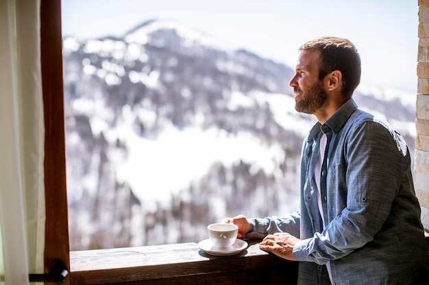 Giovane bello con una tazza di tè caldo alla finestra d'inverno