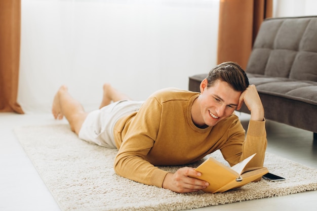 Giovane bello in abiti casual gialli seduto a casa a leggere un libro