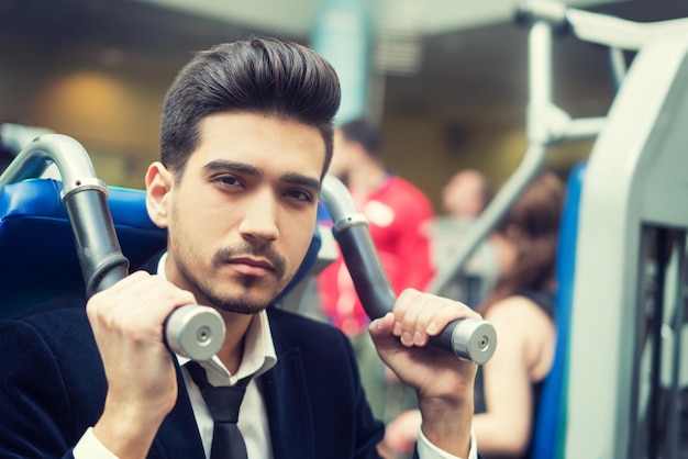 Giovane bello in un vestito nero camicia bianca e cravatta allenamento in palestra