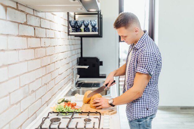 Giovane bello nell'abbigliamento casual, mentre in piedi in cucina a casa e cucinare.