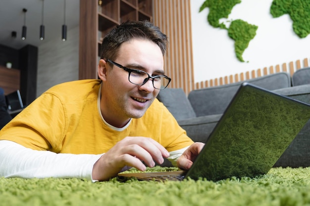 Giovane bello posa sul pavimento a casa navigando in internet sorridente