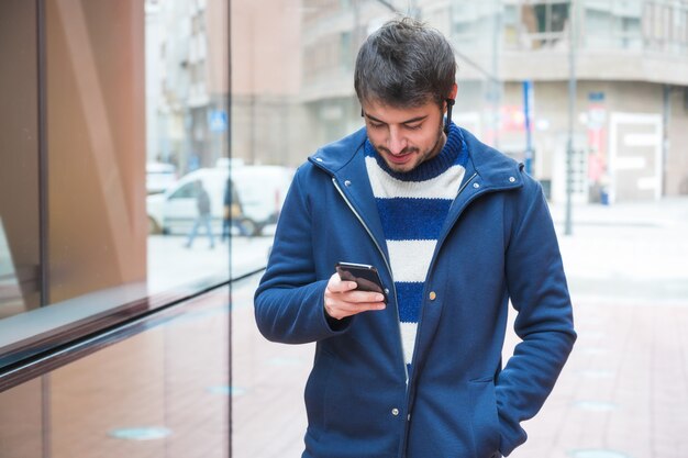 Giovane bello, stante fuori dell'edificio per uffici, facendo uso del telefono cellulare mentre avendo una pausa sul lavoro.