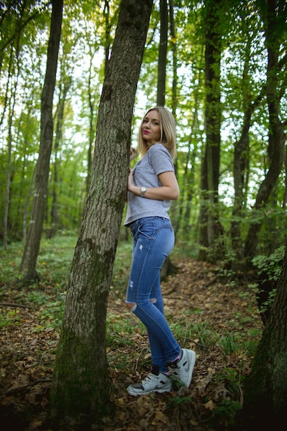 Giovane bionda donna caucasica della Bosnia-Erzegovina appoggiata all'albero e in posa