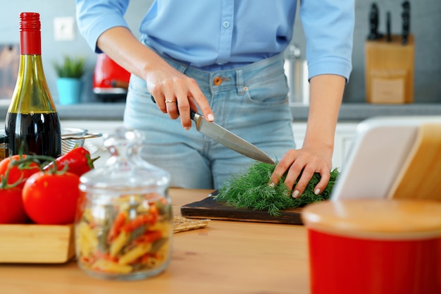 Giovane bionda donna caucasica tagliare le verdure per insalata nella sua cucina