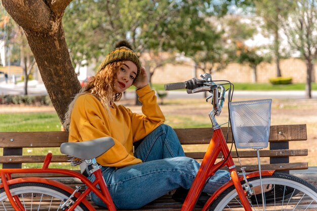 Giovane bionda seduta su una panchina, a riposo nel parco con la sua bicicletta