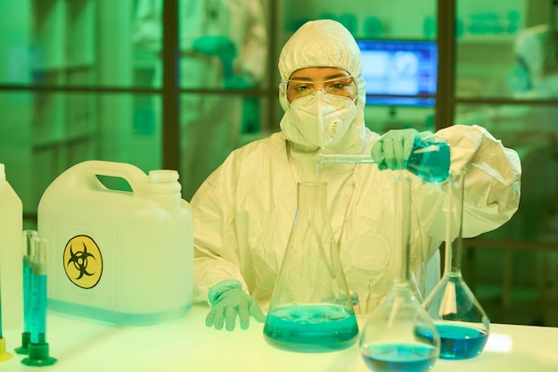 Giovane biotecnologo femminile contemporaneo che versa liquido blu nella provetta
