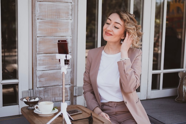 Giovane blogger bionda che lavora in un caffè di strada su un telefono cellulare