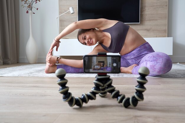 Giovane blogger femminile che registra video sportivi a casa mentre fa yoga in soggiorno