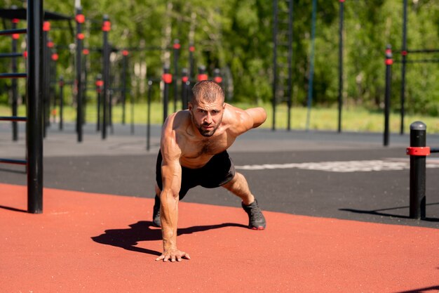 Giovane bodybuilder muscolare che si appoggia sui piedi e sulla mano destra mentre allunga il braccio sinistro all'indietro durante l'esercizio