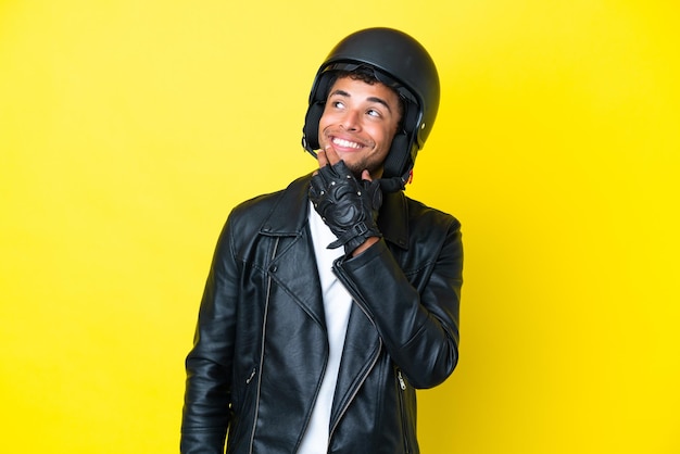 Giovane brasiliano con un casco da motociclista isolato su sfondo giallo che guarda in alto mentre sorride