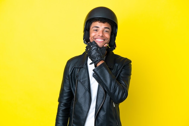 Giovane brasiliano con un casco da motociclista isolato su sfondo giallo felice e sorridente