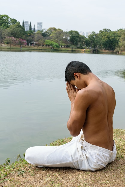 Giovane brasiliano seduto in riva a un lago in una posizione riconoscente.