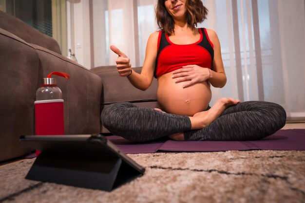 Giovane bruna caucasica incinta che dà i pollici in su all'insegnante di yoga online Esercizi online nelle lezioni di benessere durante la gravidanza