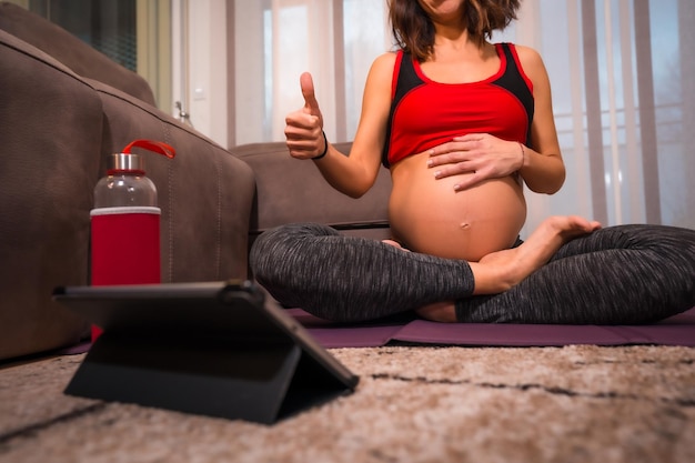 Giovane bruna caucasica incinta che dà i pollici in su all'insegnante di yoga online Esercizi online nelle lezioni di benessere durante la gravidanza