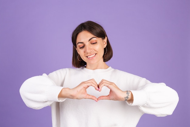 Giovane bruna in maglione casual bianco isolato sulla parete viola