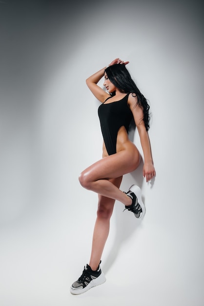 Giovane bruna sexy in un body nero su sfondo bianco. La figura atletica perfetta.
