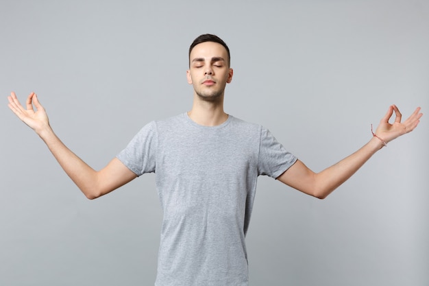 Giovane calmo in abiti casual che tiene gli occhi chiusi, si tiene per mano in un gesto di yoga rilassante meditando