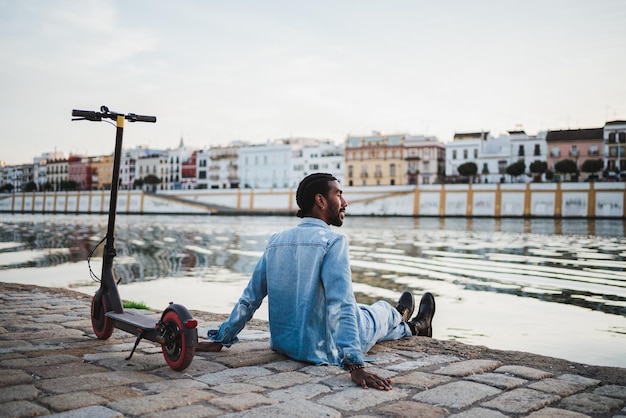 Giovane calmo seduto accanto al fiume in città Sta riposando e contemplando