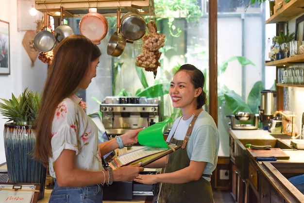 Giovane cameriera vietnamita che lavora con la macchina per il check-out e i clienti nella caffetteria