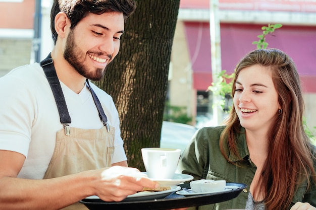 Giovane cameriere che serve caffè al cliente femminile