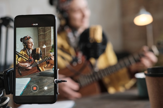 Giovane cantante che suona la chitarra e canta una canzone e la registra sul cellulare