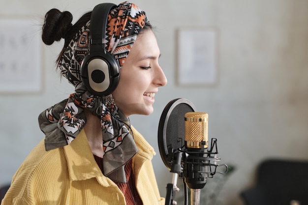 Giovane cantante in cuffia che canta nel microfono in studio di registrazione