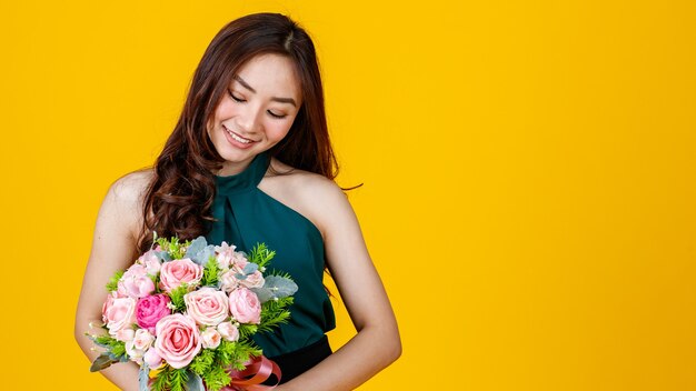 Giovane carino e capelli abbastanza ricci Asian femmina bruna holding bouquet di fiori con allegro e felice, girato in studio isolato su sfondo giallo brillante.