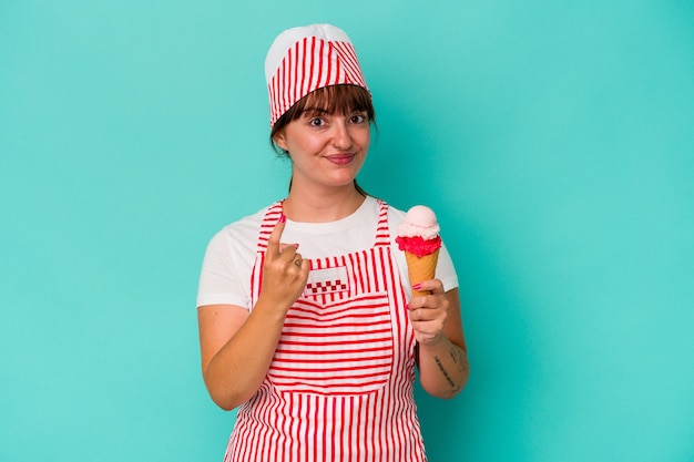 Giovane caucasica curvy gelatiera che tiene una paletta isolata su sfondo blu che punta con il dito su di te come se invitante si avvicini.