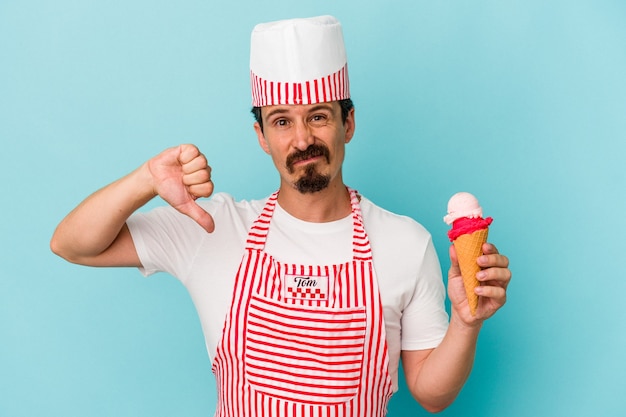 Giovane caucasica gelatiera che tiene un gelato isolato su sfondo blu che mostra un gesto di antipatia, pollice in giù. Concetto di disaccordo.