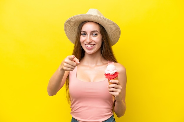 Giovane caucasico con un gelato alla cornetta isolato su sfondo giallo sorpreso e rivolto davanti