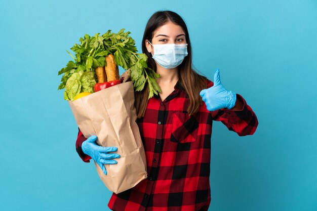 Giovane caucasico con verdure e maschera isolata sull'azzurro con i pollici in su perché è successo qualcosa di buono