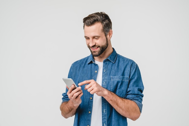Giovane caucasico felice che usa lo smartphone per chiamate, social media, applicazioni mobili online, isolato sullo sfondo bianco.