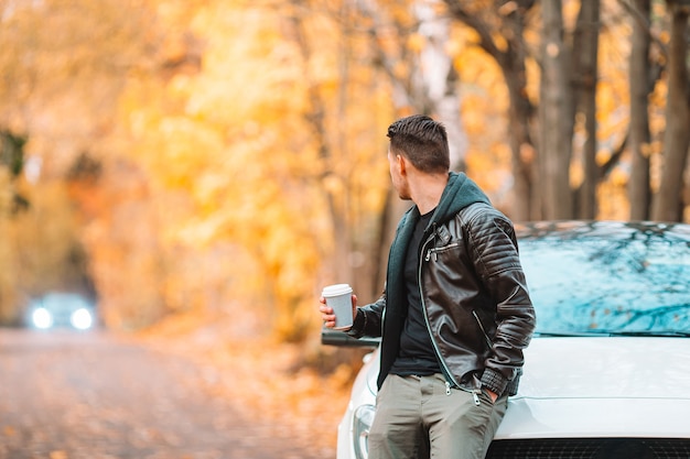 Giovane che beve caffè con il telefono in autunno parco all'aperto