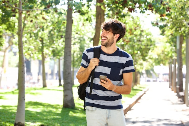 Giovane che cammina con il cellulare e la borsa nel parco