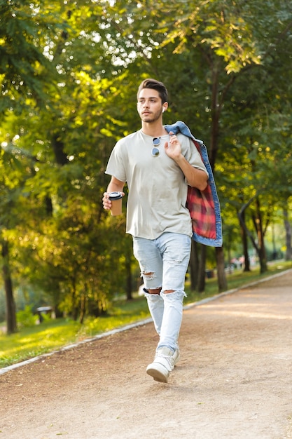 Giovane che cammina nel parco all'aperto tenendo il caffè