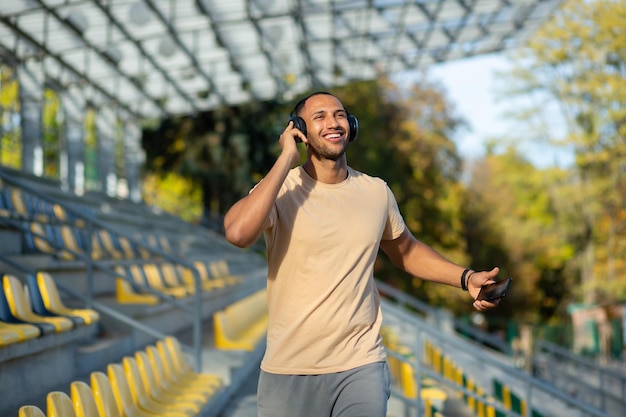 Giovane che cammina nello stadio dopo l'esercizio e fa jogging in cuffia ascoltando la musica dell'audiolibro