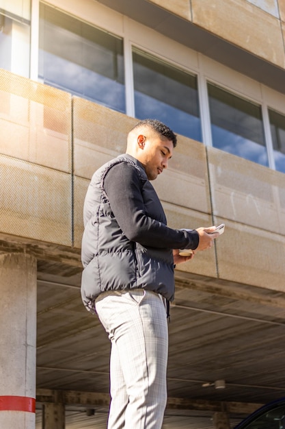 Giovane che cammina per strada con in mano un cellulare e un bicchiere di caffè Un uomo latino che cammina per strada con in mano un bicchiere di caffè e usa il cellulare