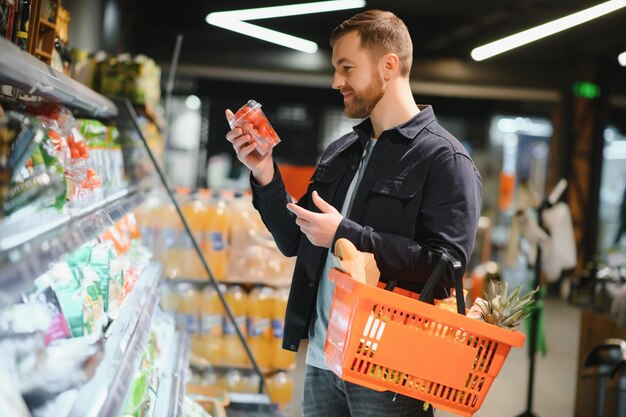 Giovane che compra generi alimentari al supermercato Altri clienti sullo sfondo Concetto di consumismo