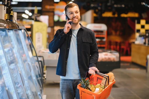 Giovane che compra generi alimentari al supermercato Altri clienti sullo sfondo Concetto di consumismo