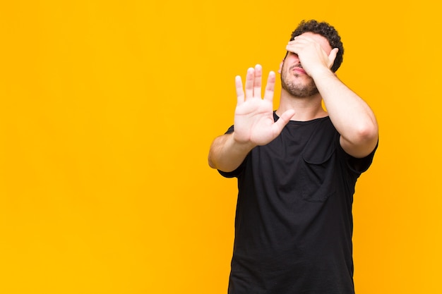 Giovane che copre il viso con la mano e mette l'altra mano davanti per fermarsi, rifiutando foto o immagini