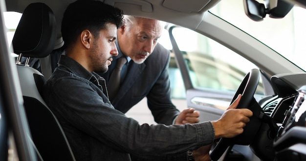 Giovane che esamina una nuova auto in uno showroom mentre il concessionario di auto sta spiegando le sue caratteristiche