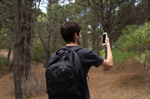 Giovane che esplora una foresta e guarda il suo telefono per indicazioni.