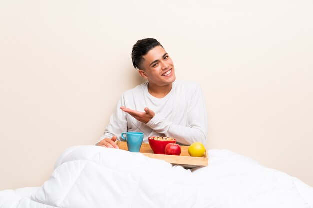 Giovane che fa colazione a letto che estende le mani a lato per l&#39;invito a venire