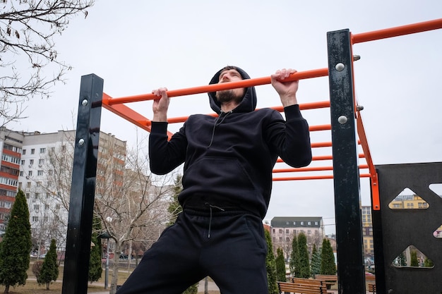 Giovane che fa esercizi di pullup sulla traversa all'aperto Esercizio sportivo fitness