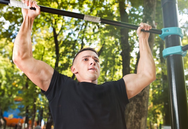 Giovane che fa pull up sulla barra orizzontale all'aperto, allenamento, concetto di sport.